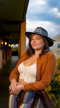 a woman wearing a hat and skirt on a balcony