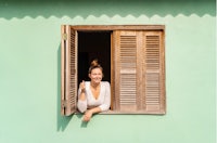 a woman leaning out of a window in a green house